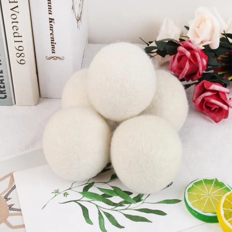 Assorted sized wool drying balls next to a beige cotton drawstring storage bag on a wooden surface.
