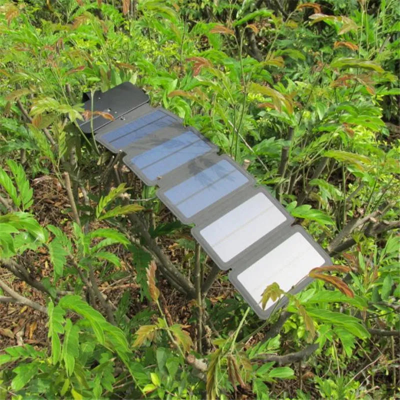 Black folding solar panel charger with monocrystalline cells and USB output, folded flat on a wooden surface, compass buckle visible