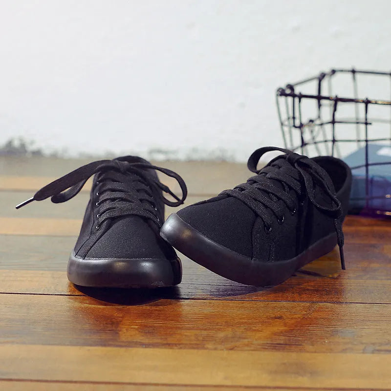 All black canvas low-top lace-up flat shoes for women on a white background