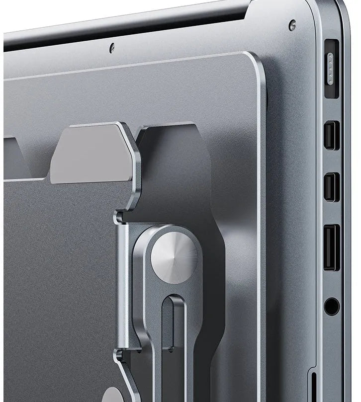 Grey aluminium laptop stand folded flat next to an open laptop, showing its adjustable angle and hollow design.