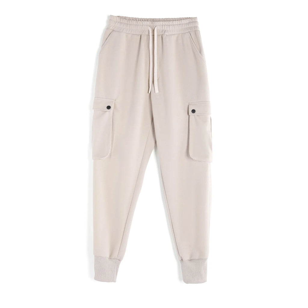 Men's loose beige cotton trousers with an ankle tie and multiple pockets on a casual model.