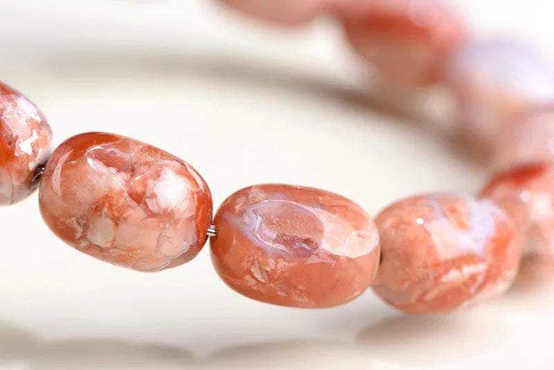Natural cherry agate barrel bead bracelet with Ruyi symbol on a wrist.