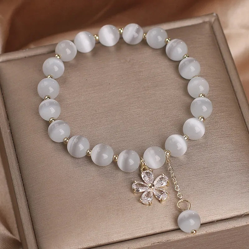 White cat's eye stone women's bracelet with flower and tassel charms on a morganite safety buckle.