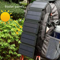 Black folding solar panel charger with monocrystalline cells and USB output, folded flat on a wooden surface, compass buckle visible