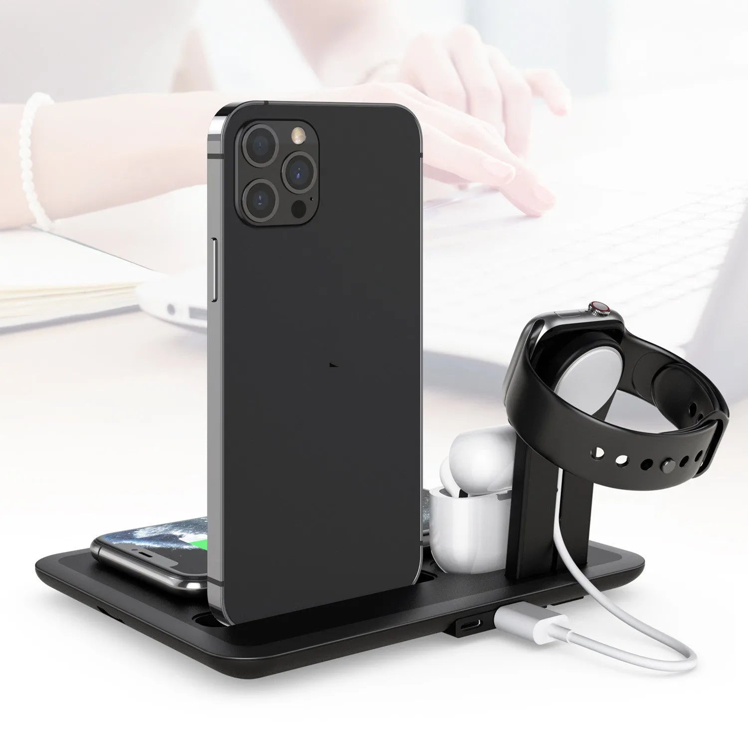 Black desktop wireless charger with phone on pad, watch and headphone cables connected.