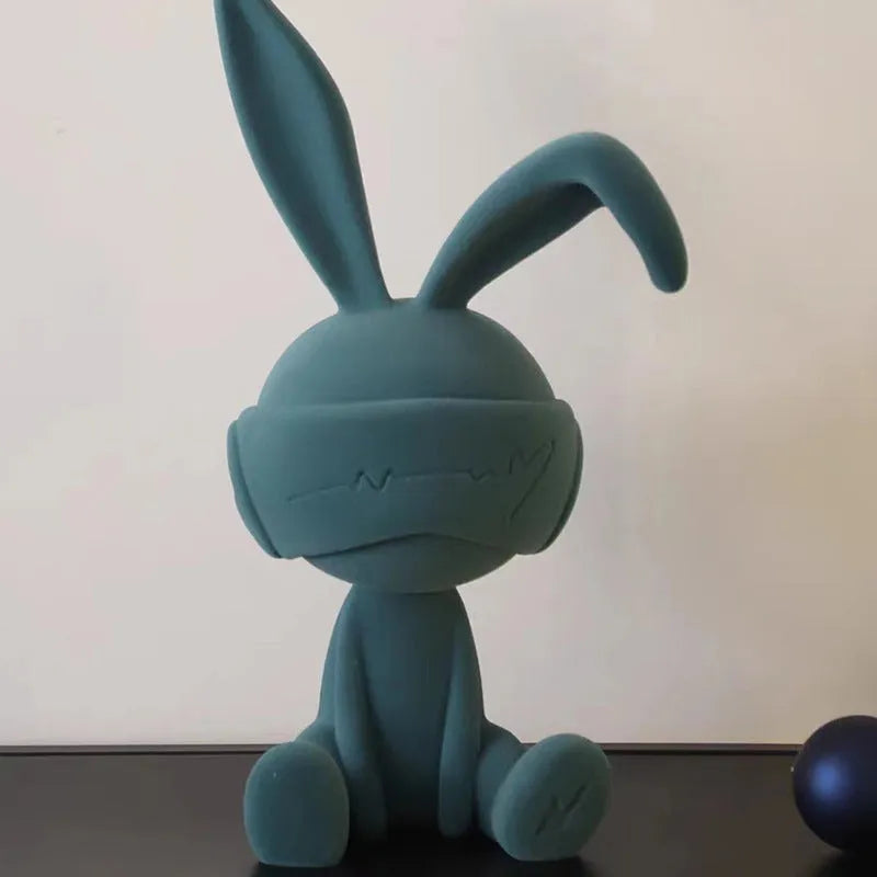 Green resin blindfold rabbit table ornament with suede details on a wooden shelf.