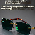 A pair of dark green frameless crystal sunglasses with a hard case and a lens cloth on a plain background.