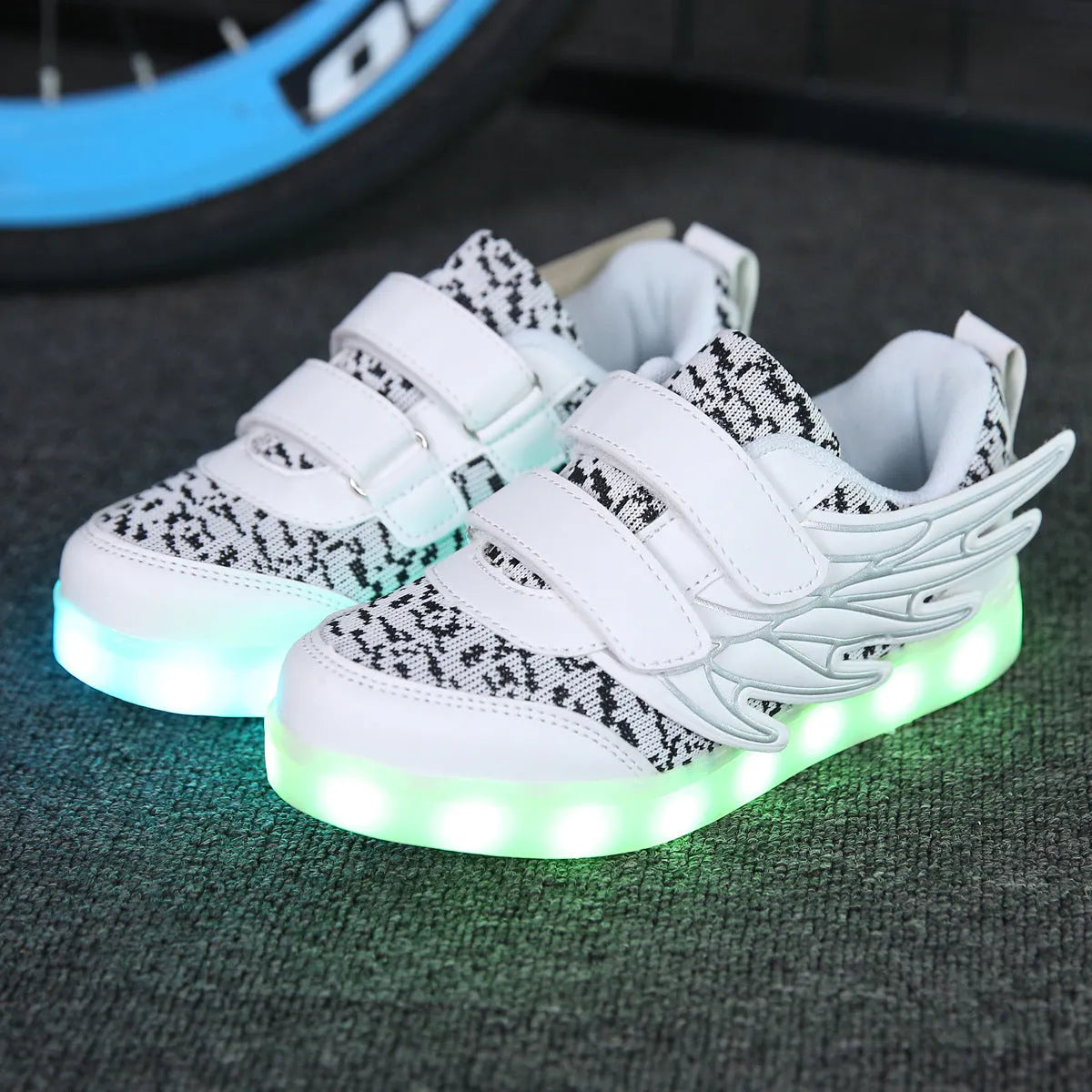 Children's plum red and white LED light-up sneakers with colourful winged lights, showing USB charging port.