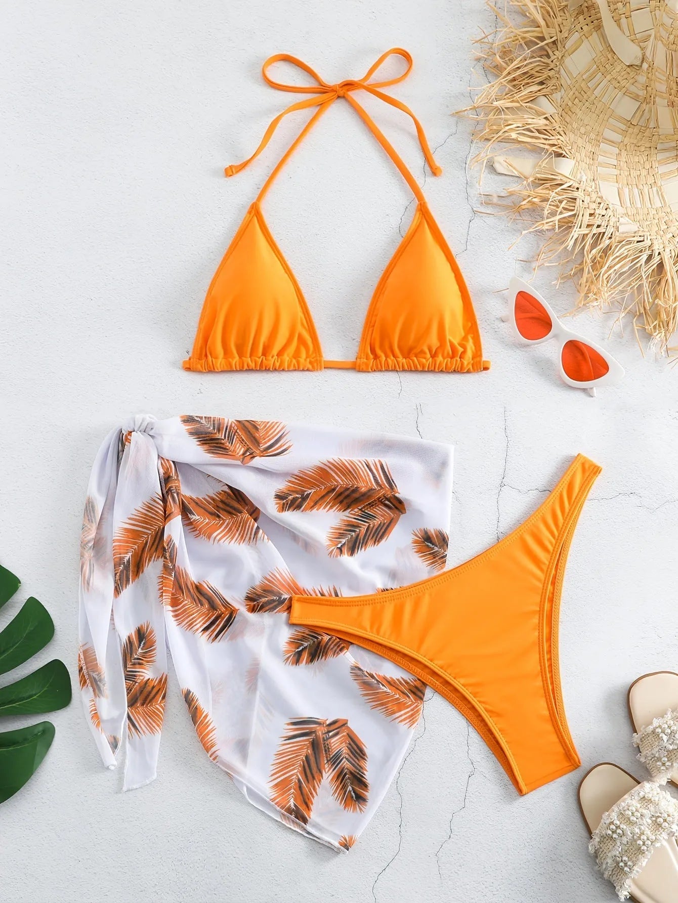 Orange three-piece bikini swimsuit set with a matching printed gauze skirt laid flat.