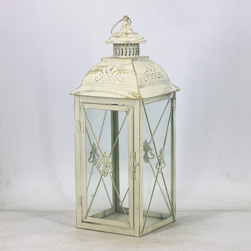 Black and white wrought iron floor standing storm lantern with tempered glass panels on a patio.