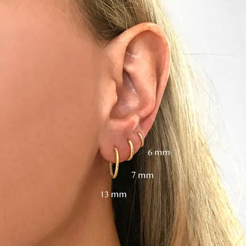 Close-up of twisted S925 sterling silver round ring earrings in gold colour on a plain background.
