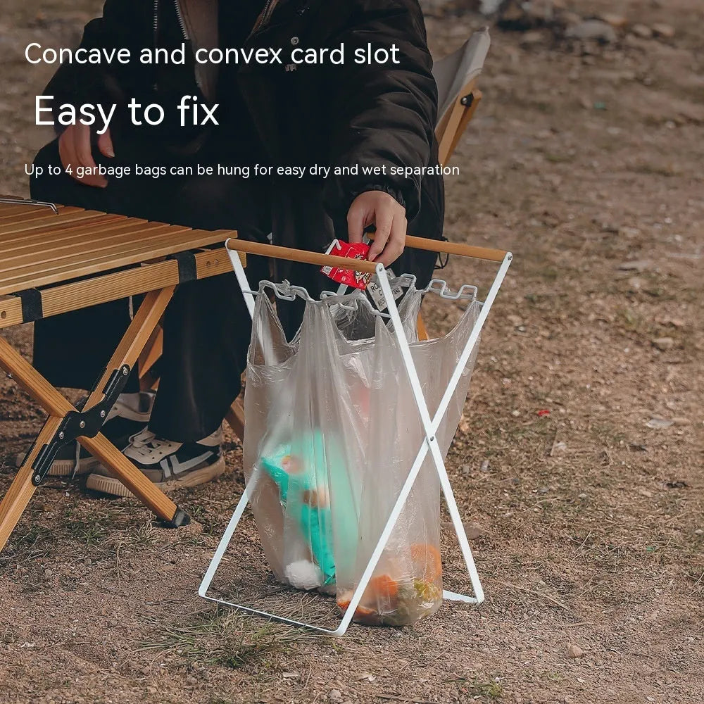 Black iron folding bin rack with wooden handles holding two rubbish bags in an outdoor setting.