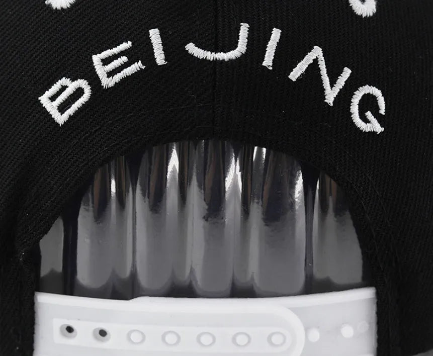 A black cotton baseball cap with embroidered lettering on the front, showing the adjustable strap at the back.