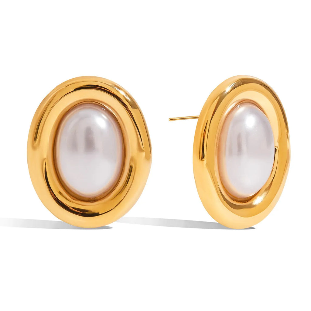 Close-up of a pair of round stainless steel stud earrings with a vintage-style pearl detail on a neutral background.