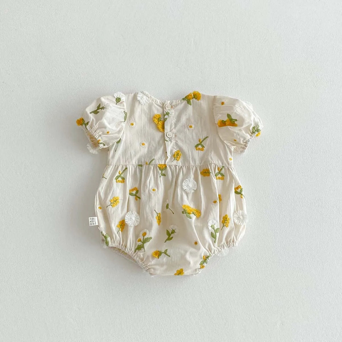 Apricot cotton baby romper with embroidered sunflower, short sleeves, triangle jumpsuit shape and hidden hook closure.